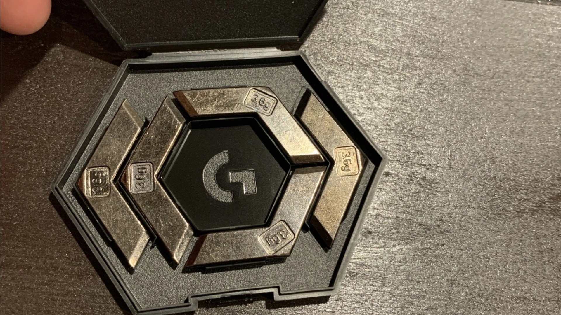 Hexagonal case containing several weighted pieces, each labeled with a gram weight, arranged in a precise pattern.