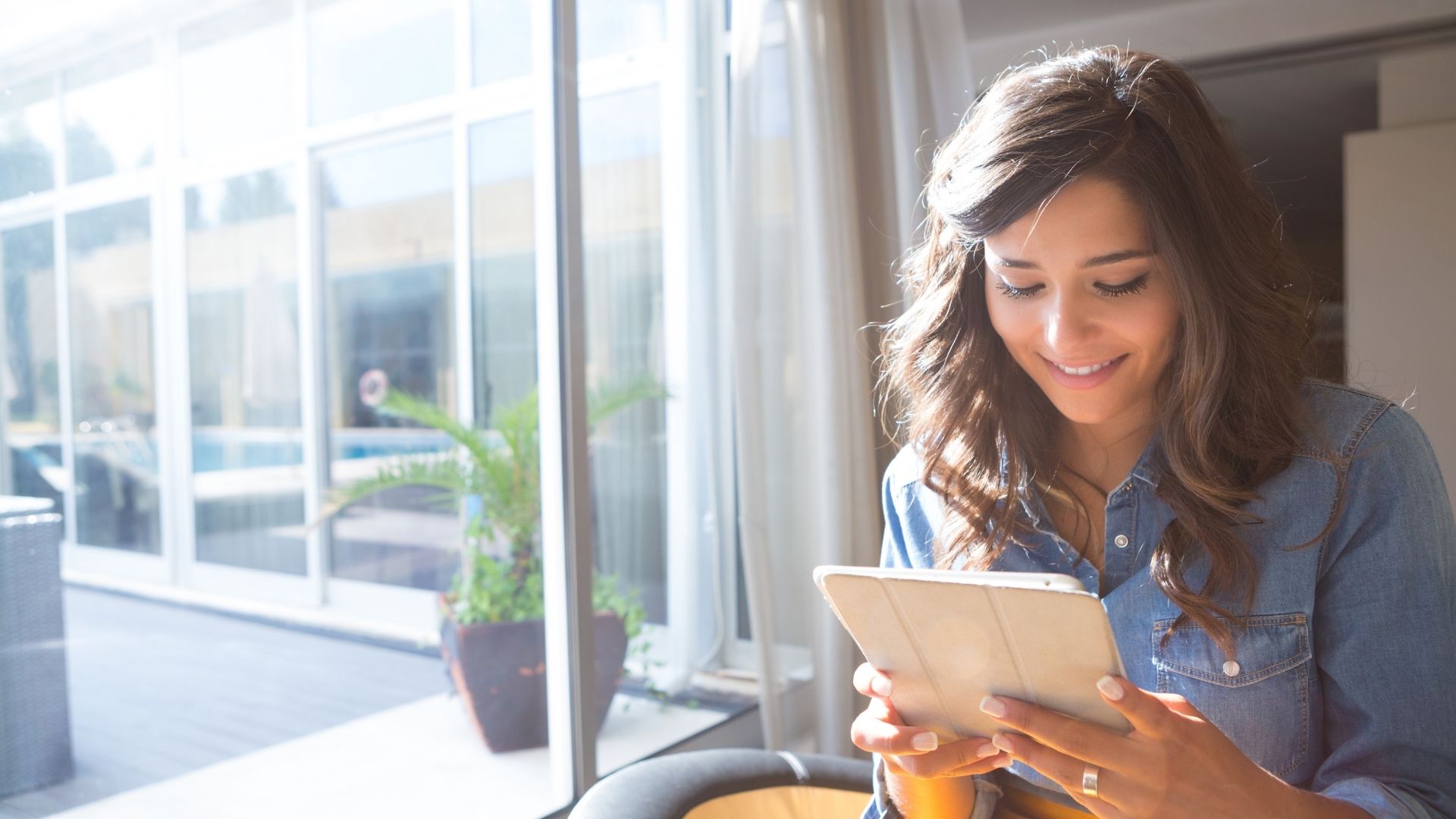 Woman using a tablet computer by a large window overlooking a patio.