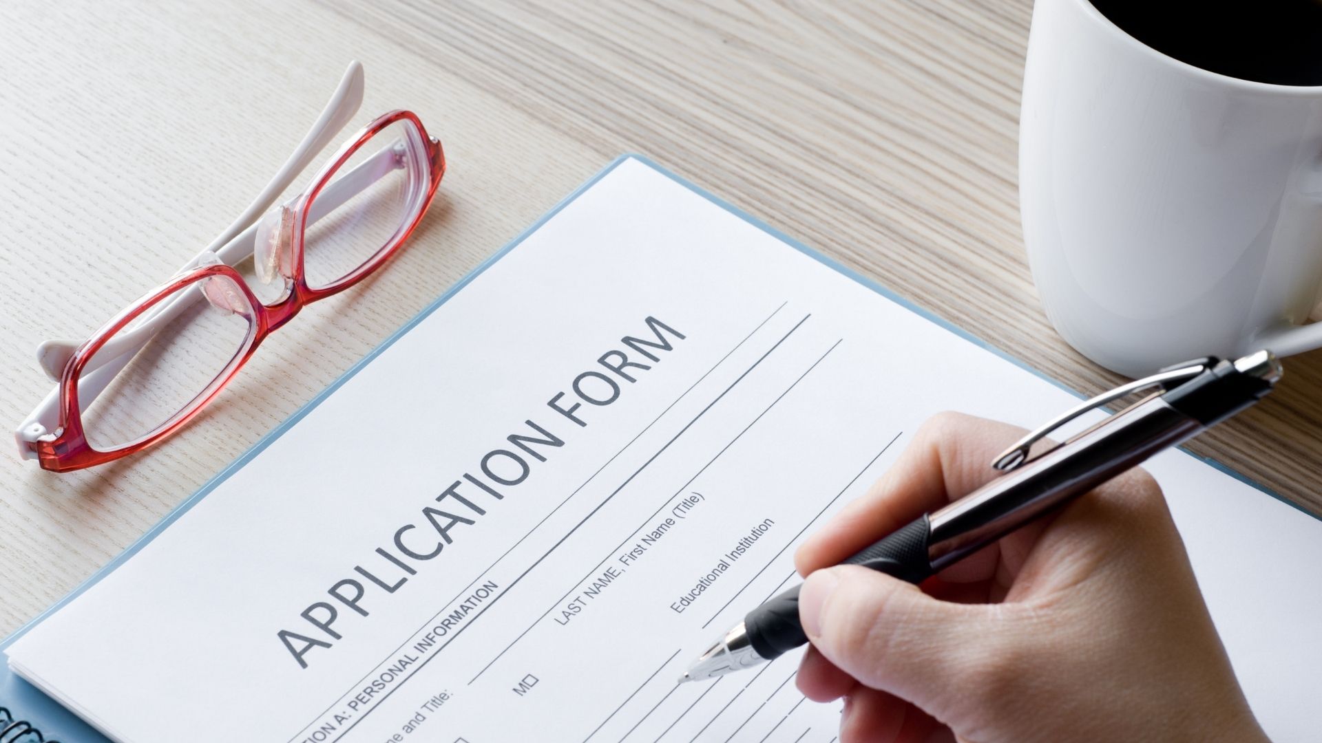 Application form with pen, glasses, and coffee cup, ready to be filled out.