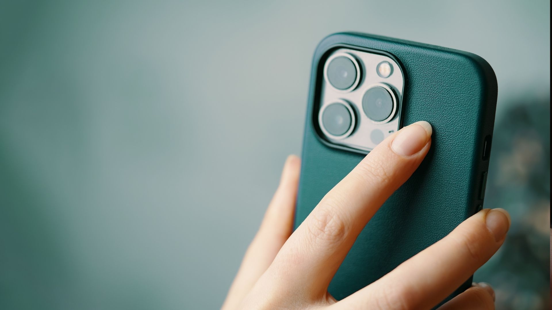 Close-up of a hand holding a teal-colored smartphone case with multiple camera lenses.